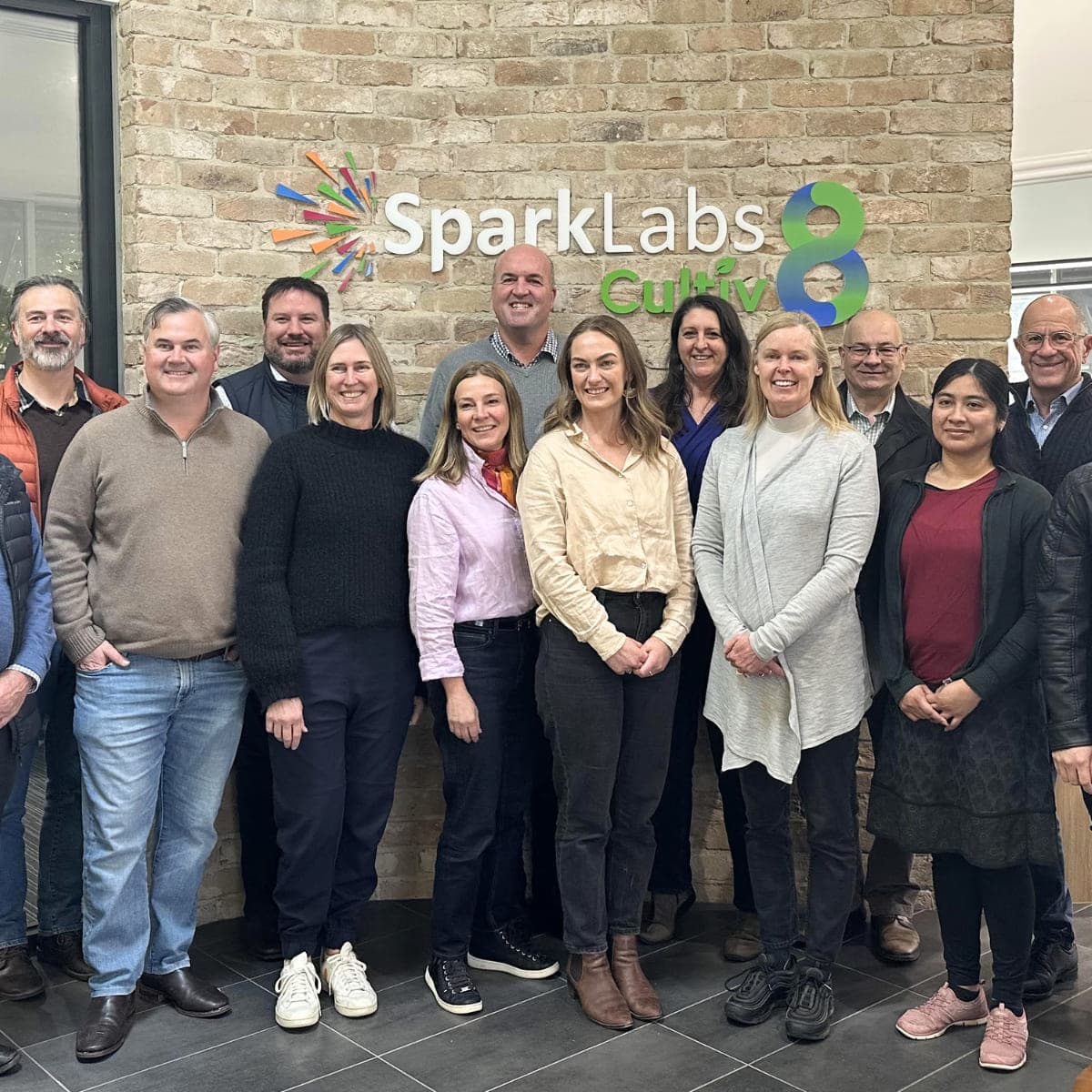 The SparkLabs Cultiv8 team standing together in front of a brick wall carrying the Cultiv8 mark