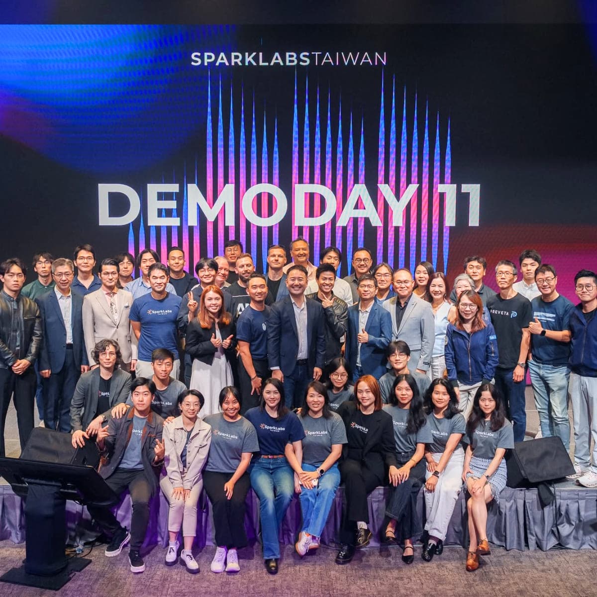 The SparkLabs Taiwan cohort assembled on stage in front of the Demoday 11 screen