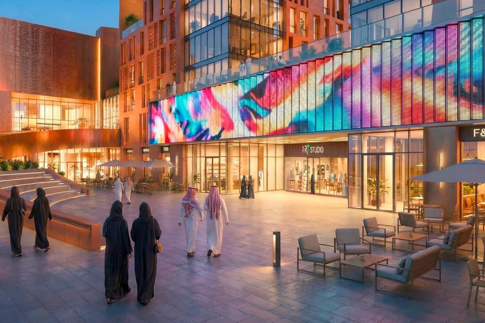 Architectural render of the Riyadh Creative Hub at dusk: people crossing a stone plaza beneath a long, colour-lit media facade, with an art studio and cafe terraces at street level